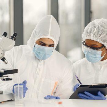 Scientists and microbiologists with PPE suit and face mask hold test tube and microscope in lab, finding treatment or vaccine for coronavirus infection. Covid-19, laboratory, and vaccine concept.